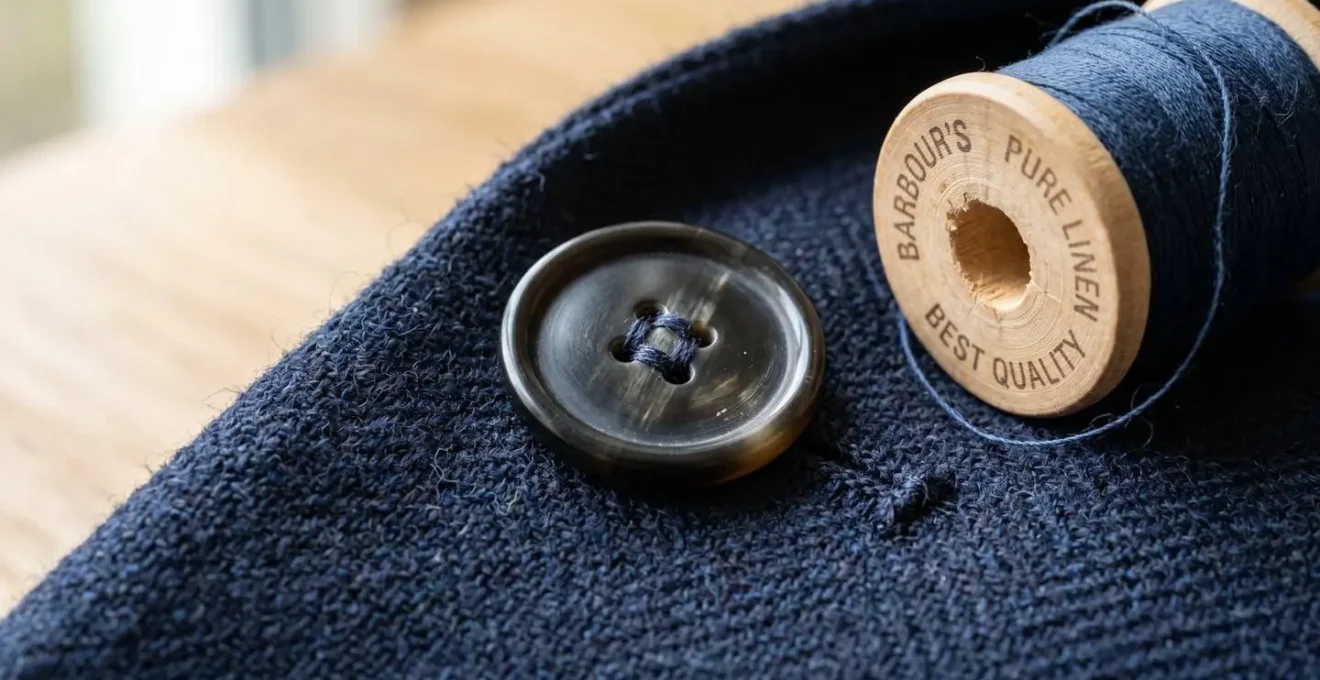 Gros plan sur la texture d'un tissu de costume en laine anthracite, avec des fils de couture et un bouton en corne posés sur le tissu